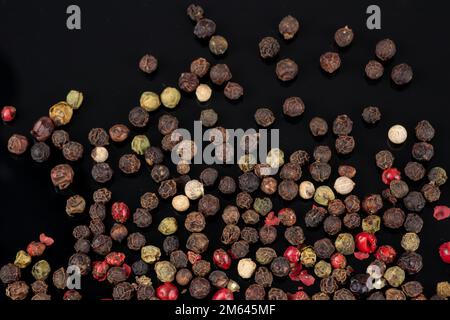 I peperoni colorati in pile si mescolano su sfondo nero. Foto Stock