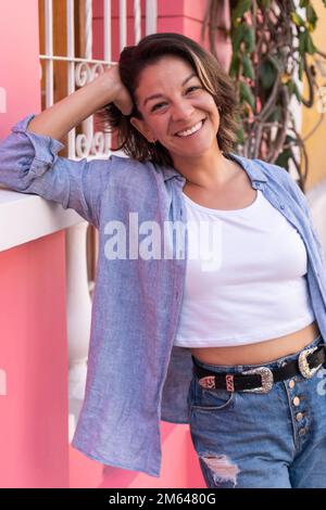 Donna ispanica appoggiata contro una parete rosa Foto Stock