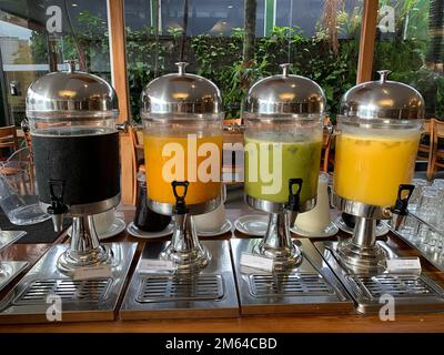 Quattro erogatori di succo trasparenti con rubinetto riempito con succhi colorati Foto Stock