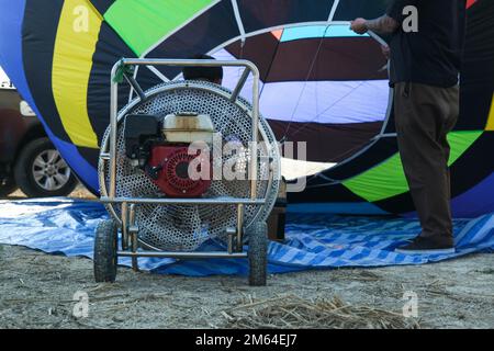 Guardando all'interno mongolfiera mentre si è a terra e preparandosi per un volo. Un pilota di palloncino gonfia un palloncino ad aria calda con una ventola grande mentre un wic Foto Stock