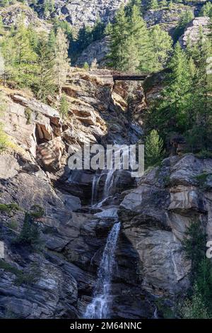 Cascata Alpina di Lillaz (Cascate di Lillaz) su 3 livelli accessibile attraverso un dolce sentiero con ponte di legno ondoso, vista dal basso. Cogne, Valle d'Aosta Foto Stock