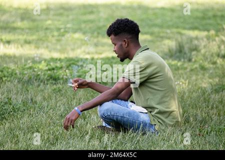 il giovane fuma seduto sull'erba nel parco cittadino Foto Stock