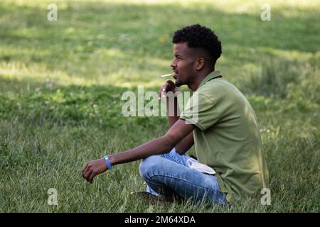 il giovane fuma seduto sull'erba nel parco cittadino Foto Stock