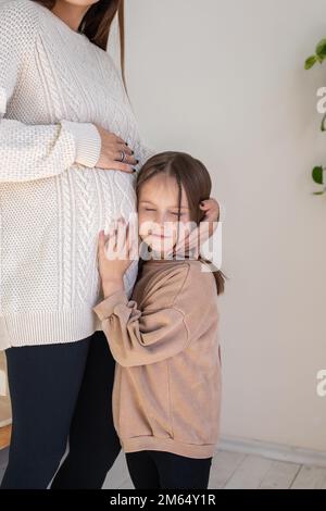 Ragazza carina che ascolta le mosse del bambino nel ventre delle mamme incinte Foto Stock