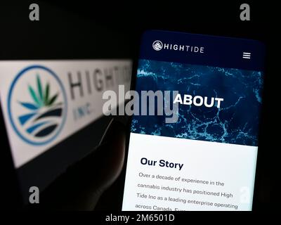 Persona che tiene il cellulare con il sito web della società canadese di cannabis High Tide Inc. Sullo schermo di fronte al logo. Messa a fuoco al centro del display del telefono. Foto Stock