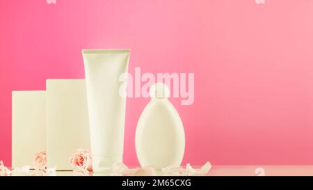 Mock up di prodotti naturali di bellezza a base di fiori di rosa. Tubo cosmetico bianco e bottiglia con scatole bianche su fondo a gradiente rosa con rosa tenera Foto Stock