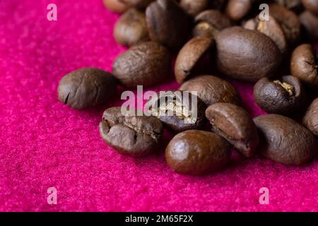 Immagine ravvicinata dei chicchi di caffè tostati di colore marrone fresco su sfondo magenta vivo. CopySpace in basso a sinistra. Foto Stock