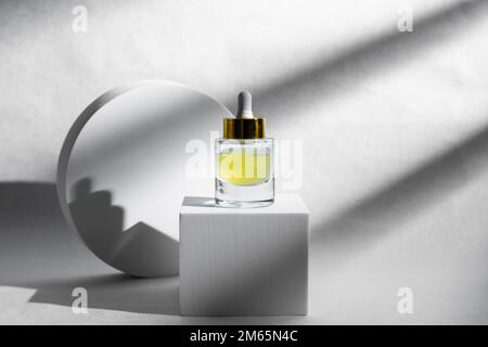 Concetto di bellezza alla moda dei sieri facciali, olio essenziale naturale in bottiglie cosmetiche con contagocce e luminosa ombra solare su sfondo bianco. Foto Stock