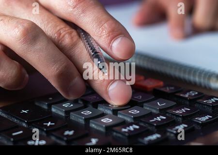 Analisi dei dati finanziari. Foto ravvicinata della mano di un uomo d'affari che scrive e conta sulla calcolatrice in ufficio Foto Stock