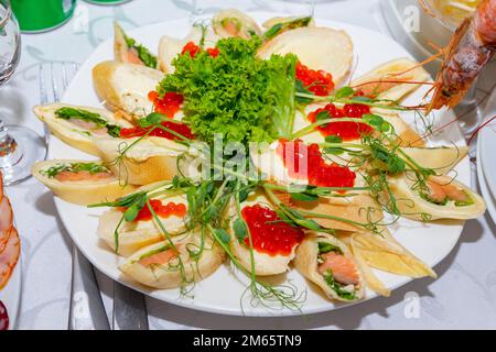 I pancake con pesce rosso e caviale rosso sono decorati con verde. Spuntini freddi sul tavolo festivo Foto Stock