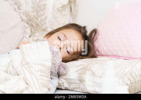 Bella bambina che dorme sul letto sotto la coperta con orsacchiotto. Ritratto di bambino addormentato. Mattina, abbia sogno dolce. Dormi con il giocattolo imbottito preferito. Foto Stock