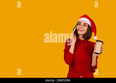 Giovane donna CREERful a Santa Hat che ha conversazione telefonica Foto Stock