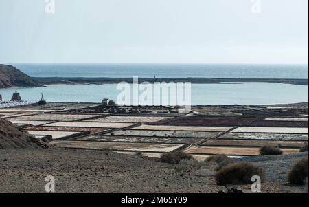 La vista dall'alto delle saline di Lanzarote. Il contrasto tra la laguna color smeraldo e i grani neri della spiaggia è così sorprendente. Foto Stock