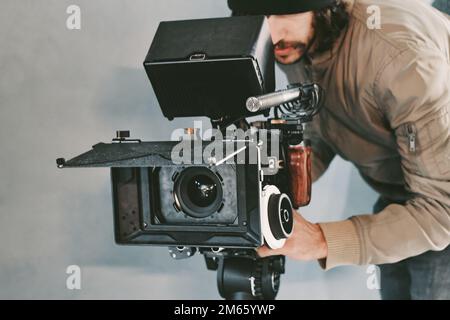 Un giovane cameraman maschio dietro una videocamera cinematografica che riprende sul set Foto Stock