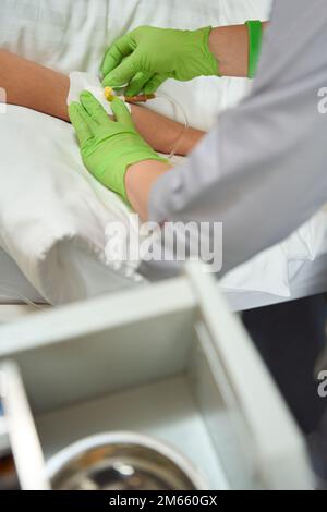 L'infermiere usa l'intonaco quando fissa l'ago alla mano del paziente Foto Stock