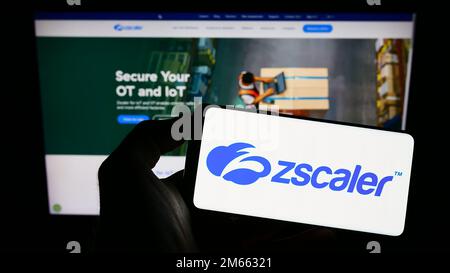 Persona che tiene in mano uno smartphone con il logo della società statunitense di sicurezza sul cloud Zscaler Inc. Sullo schermo di fronte al sito Web. Messa a fuoco sul display del telefono. Foto Stock