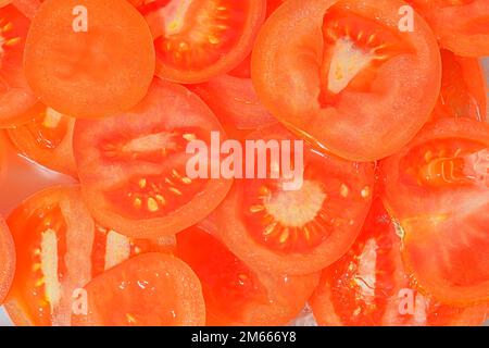 Fette di pomodoro in acqua su fondo bianco. Primo piano di pomodoro in liquido con bolle. Fette di pomodoro rosso maturo in acqua. Immagine macro di verdure in Foto Stock