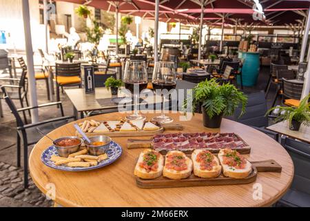 Un primo piano di antipasti di vino vicino a due bicchieri di vino su un tavolo di legno in un caffè Foto Stock