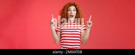 OMG affascinante negozio controllare. Impressionato eccitato buon-osservare redhead arricciamente emotivo ragazza goccia mascella stupito felice che punta sulle dita dell'indice Foto Stock