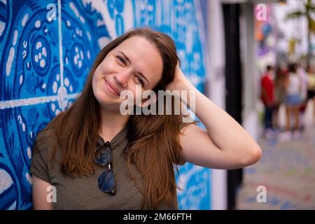 Giovane e bella donna si appoggia contro un muro colorato e si pone per la macchina fotografica - stile di strada tipico Foto Stock