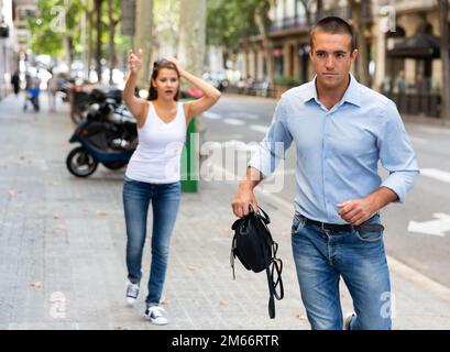 Bandit uomo che corre con la borsa dopo rubato questo da emotivo femmina Foto Stock