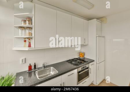 una cucina con armadi bianchi e piani di granito nero al centro dell'immagine è un forno, lavastoviglie, lavello Foto Stock