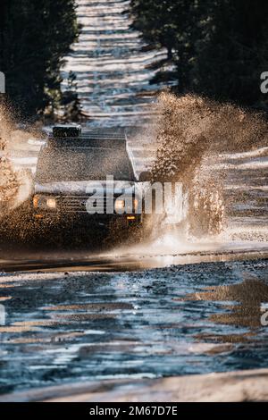 Vista frontale ad angolo del SUV fuoristrada Overland Land Cruiser che attraversa l'acqua su un sentiero innevato nella foresta Foto Stock