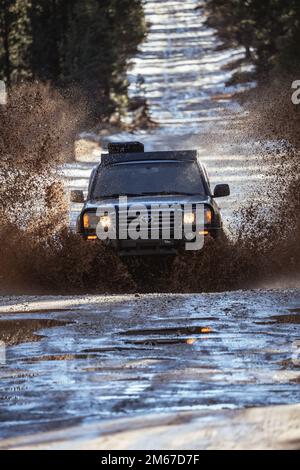 Vista frontale ad angolo del SUV fuoristrada Overland Land Cruiser che attraversa l'acqua su un sentiero innevato nella foresta Foto Stock