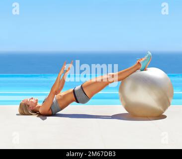 Shes in condizione fisica di picco. una giovane donna attraente che si alleni con una palla da ginnastica presso una piscina. Foto Stock