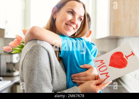 Figlio si congratula con la mamma e dà la sua carta e un bouquet di fiori ai tulipani Foto Stock