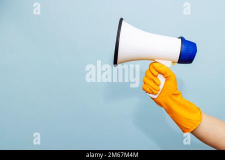 Mano in guanto di protezione in gomma gialla con megafono su sfondo blu Foto Stock