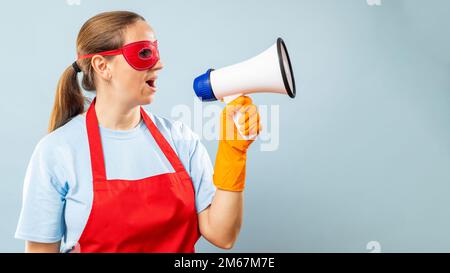 Donna con maschera rossa, guanti e grembiule con megafono su sfondo blu Foto Stock