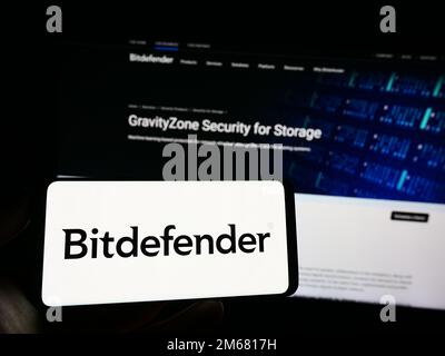 Persona che tiene il telefono cellulare con il logo della società rumena di cybersicurezza Bitdefender sullo schermo di fronte alla pagina web. Messa a fuoco sul display del telefono. Foto Stock