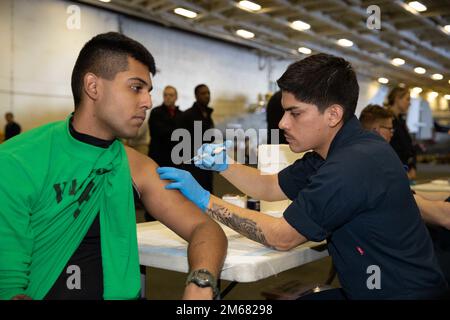 L'Hospitalman Michael Mino, di destra, di Newark, New Jersey, assegnato al dipartimento medico della USS Gerald R. Ford (CVN 78), amministra un vacine all'Aviazione strutturale meccanica Airman Apprentice Leonardo RamosRosado, di Sterling, Virginia, assegnato allo Electronic Attack Squadron (VAQ) 142, durante una valutazione periodica della salute nella baia di hangar, aprile 15, 2022. Ford è in corso nell'Oceano Atlantico che conduce le qualifiche dei vettori e l'integrazione dei gruppi di sciopero prima dello spiegamento operativo. Foto Stock