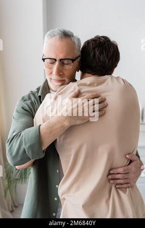 uomo anziano con gli occhi chiusi che abbraccia il figlio adulto a casa, immagine di scorta Foto Stock