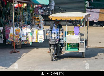 SAMUT PRAKAN, THAILANDIA, ottobre 19 2022, un distributore di gelati guida una moto a tre ruote lungo una strada cittadina Foto Stock