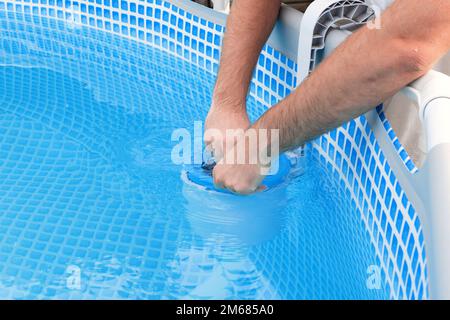 L'uomo pulisce lo skimmer per la piscina di telaio. Pulizia piscina contaminata. Foto Stock