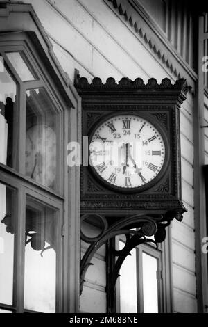 Vecchio, nostalgico orologio da parete all'aperto alla stazione ferroviaria, vista verticale. Conversione monocromatica. Foto Stock