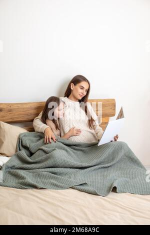 Giovane donna incinta e una bambina sul letto che guarda tranquillo Foto Stock