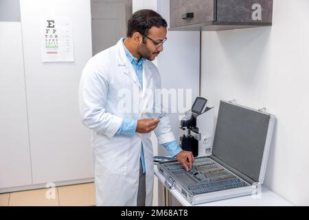 Medico di sesso maschile in camice da laboratorio in piedi la scatola con attrezzatura optometrica Foto Stock