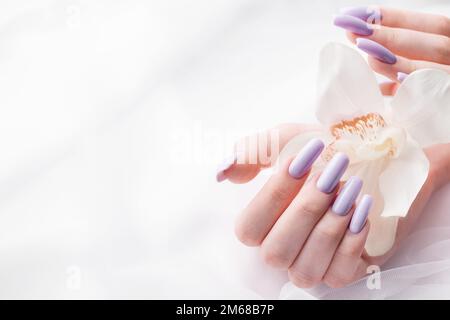 Mani di ragazza con delicata manicure viola e fiori di orchidea. Il concetto di bellezza e cura del corpo. Foto Stock