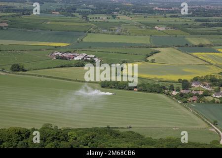 Un veicolo agricolo che sparge fertilizzante artificiale su un coltivatore arabile in una giornata ventosa vicino a Roseberry Topping nel North York Moors Foto Stock