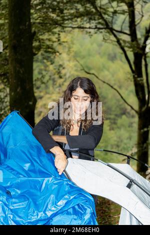 Giovane uomo con outdoor attrezzatura messa in piedi la sua tenda in una radura dopo una giornata di escursioni nel bosco Foto Stock