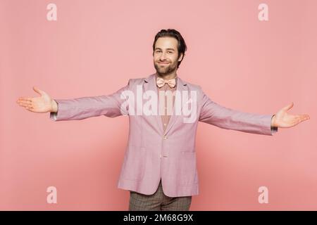 Ospite positivo di evento in cravatta d'arco e giacca outstretching mani isolato su rosa, immagine stock Foto Stock