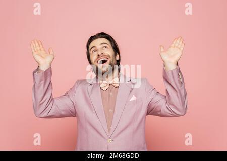 Allegro ospite di evento in giacca e tuta guardando su sfondo rosa, immagine stock Foto Stock
