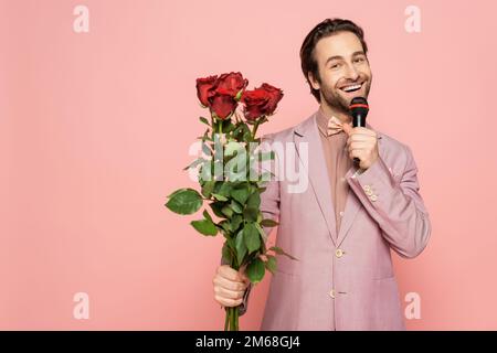 Allegro ospite di evento con microfono e bouquet di rose isolato su rosa, immagine stock Foto Stock