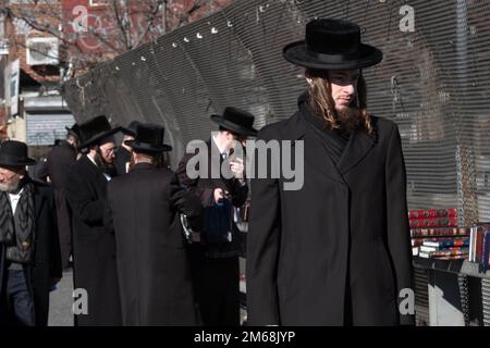 Una scena di strada a Brooklyn di acquirenti e passanti che passeggiando davanti a una pop up vendita di libri religiosi ebrei. Foto Stock