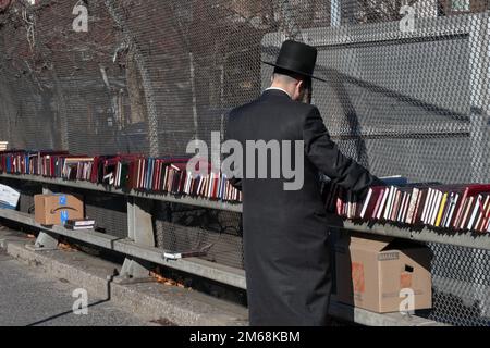 Un uomo ebraico hassidico non identificabile fa shopping di libri in una vendita di libri a Brooklyn, New York, in una mite giornata invernale. Foto Stock