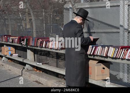 Un uomo ebraico hassidico con lunghi negozi di peyus per libri religiosi in un negozio pop-up a Brooklyn in una mite giornata invernale. Foto Stock