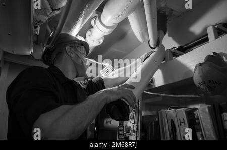 YOKOSUKA, Giappone (19 aprile 2022) – l'Operations Specialist Seaman Jacob Dess, di West Palm Beach, Fla., rimuove la schiuma danneggiata da un tubo a bordo della nave ammiraglia US 7th Fleet USS Blue Ridge (LCC 19) 19 aprile 2022 a Yokosuka, Giappone. Il ritardo è utilizzato come isolamento termico per tubi e paratie all'interno della nave. Blue Ridge è la più antica nave operativa della Marina militare e, come la 7th Fleet Command ship, lavora attivamente per promuovere le relazioni con alleati e partner nella regione di Indo-Pacifico. Foto Stock